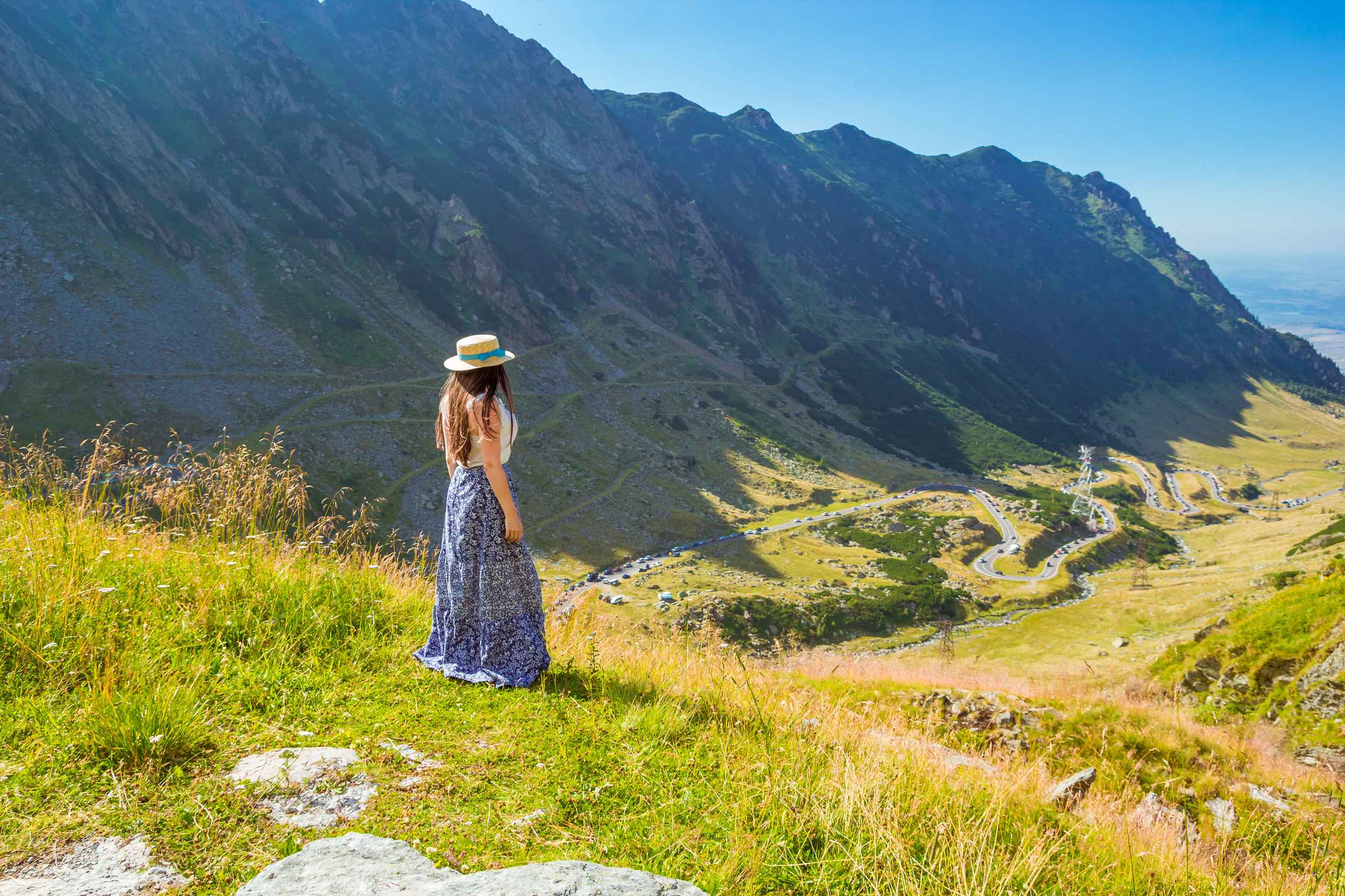 A Girl In Straw Hat And Dress Looking From High At The Transfagarasan Alpine