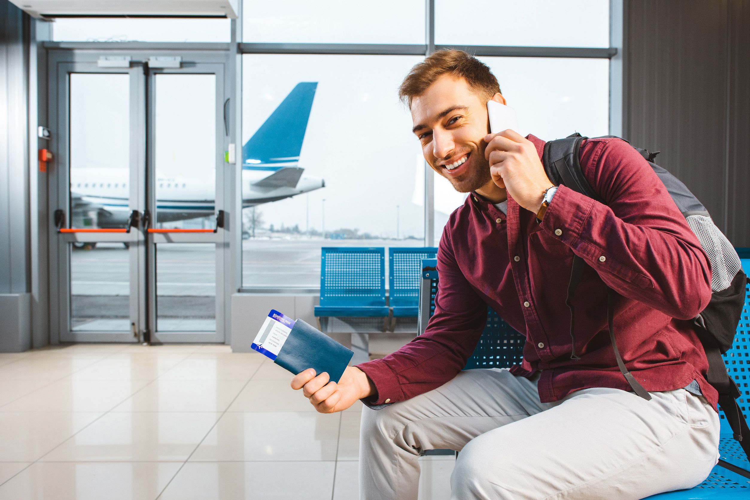 Smiling Man Talking On Smartphone While Sitting In Airport