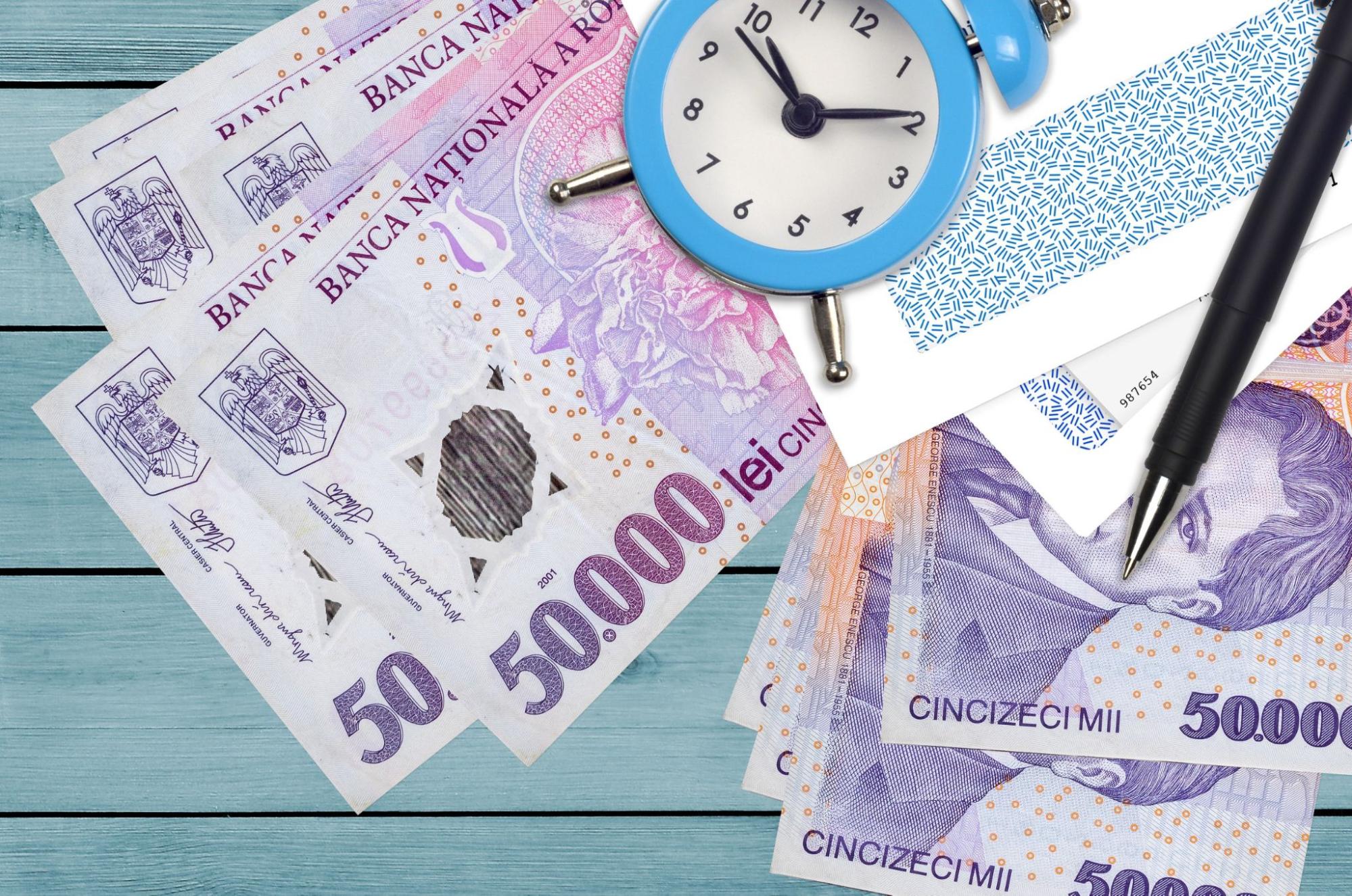 50,000 Romanian leu bills and alarm clock with pen and envelopes. Tax season concept, payment deadline for credit or loan