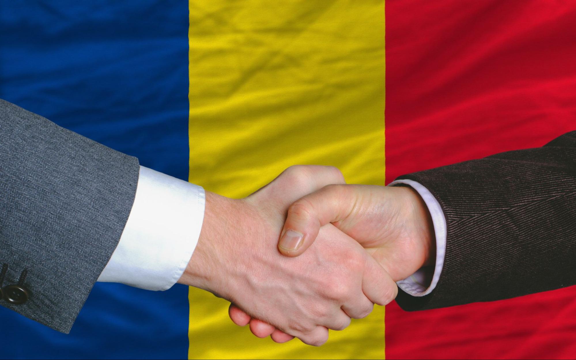 Two businessmen shaking hands after good business investment agreement in romania, in front of flag